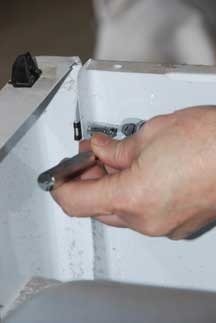 Man's hand unscrewing a clothes dryer’s front lower kick plate panel.