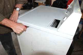 Man's hands opening a white clothes dryer's topside with a knife. 