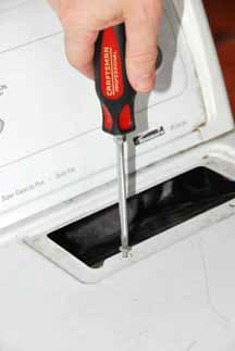 Man's hand unscrewing a clothes dryer's top cover.