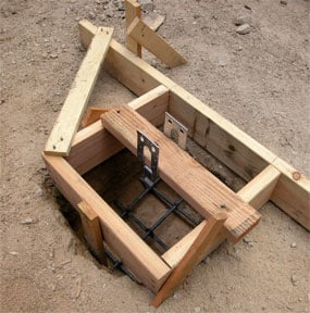Square concrete pier mold made of lumber scraps including a reinforcing bar under and side supports.