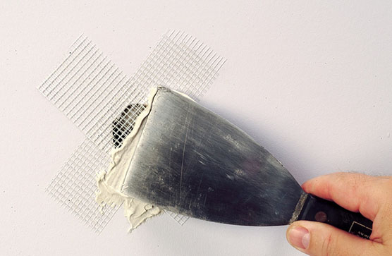 Patching hole in drywall by applying spackling compound over fiberglass mesh tape