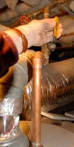 Hand reaching for the lever of a water supply valve above a water heater.