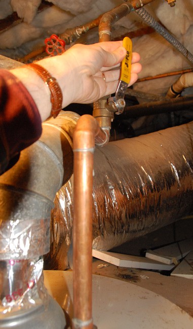 Man's hand holding a lever valve above a water heater.