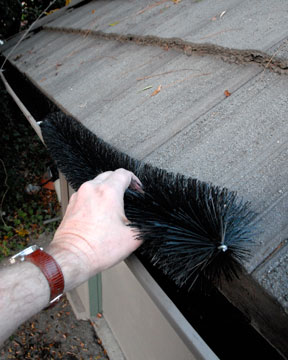 Man's hand taking out a black, long brush from a gutter.