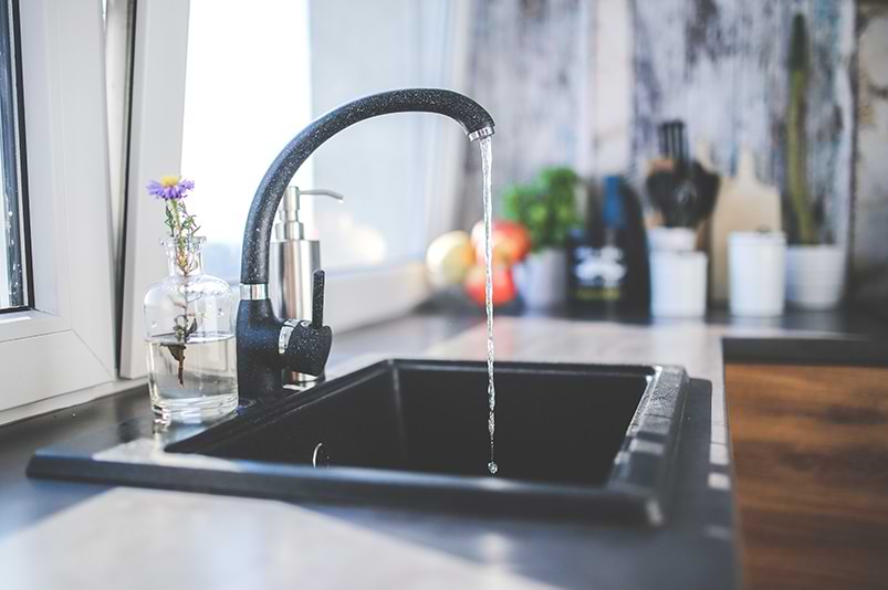 A black kitchen faucet with water running.