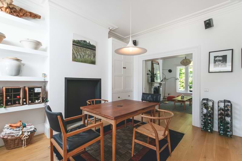 A room with wood floor, wooden table set, and white walls.