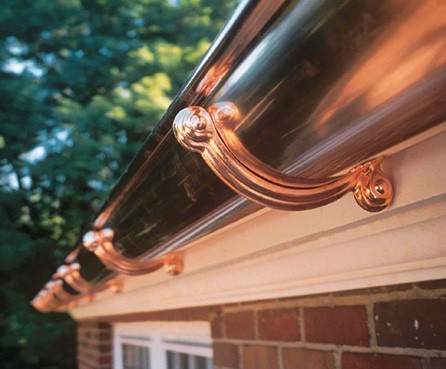 Half-round sophisticated copper rain gutter with brackets in a house’s roof.