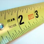 Close-up view of a yellow steel-type measuring tape, over a white background.