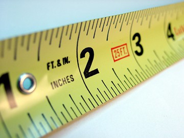 Close-up view of a yellow steel-type measuring tape, over a white background.