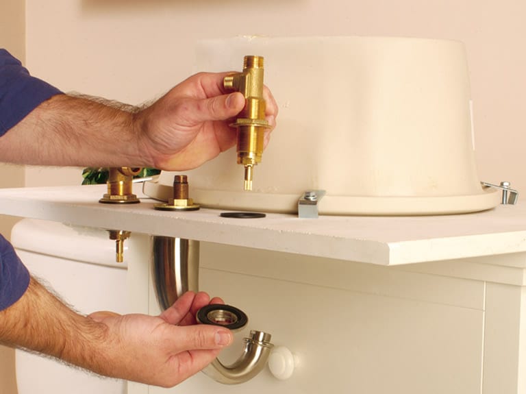 Man installing the faucet body and valve components of a bathroom sink. 