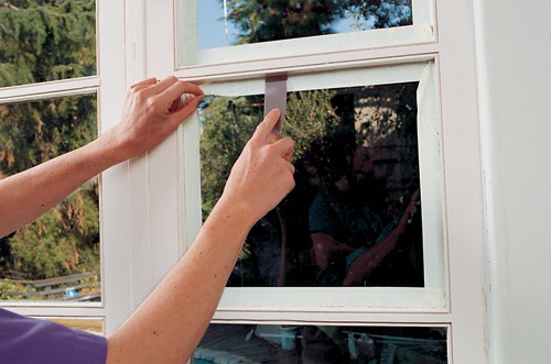 Woman's hands sealing a window pane's masked corner using a putty knife.