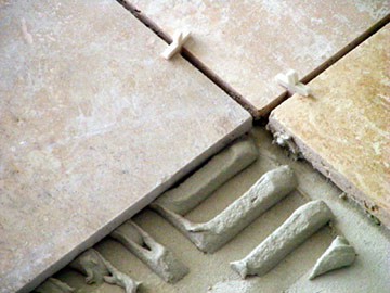 Close-up view of gray thinset mortar beneath stone tiles, with cross-type spacers.