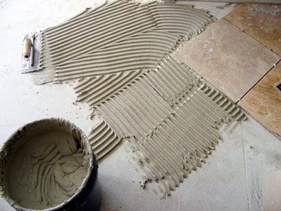 Tile installation with a bucket of mixture and layer of combed mortar.