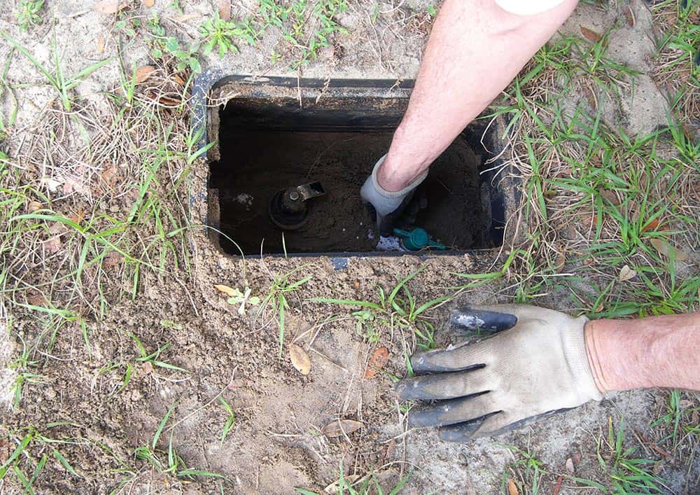 A gloved hand reaching into an underground water shutoff box.