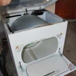 Man’s hand lifting a white clothes dryer's top cover.