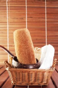 A large wooden ladle, luffa sponge, and towel in a rattan basket.