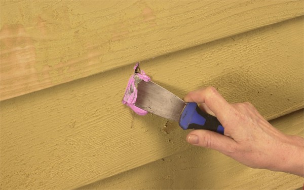 A hand patching holes in wood siding with exterior spackling compound.