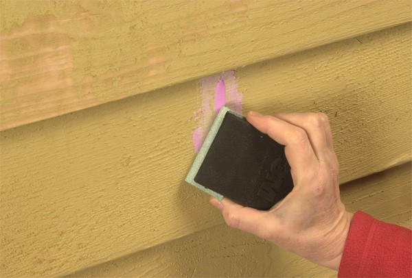 Hand sanding dried spackling compounding on a patched area of wood siding.