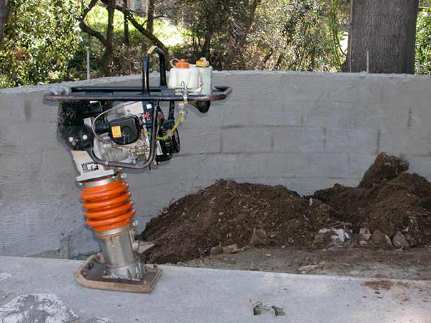 motorized soil compactor standing next to loose soil