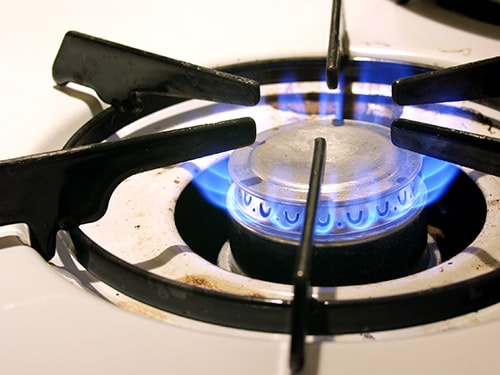 A gas burner's cooktop emitting a blue flame.