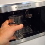 Hand holding a glass under an ice maker.