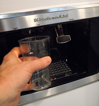 Hand holding a glass under an ice maker.