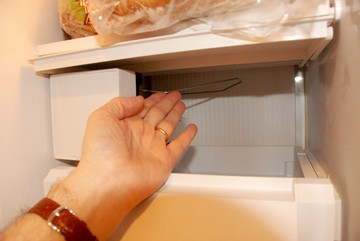 Hand holding setting the bail wire of an ice maker to the OFF position.