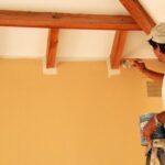 Man painting the corner of a ceiling and wall using a brush.
