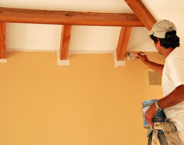 Man painting the corner of a ceiling and wall using a brush.
