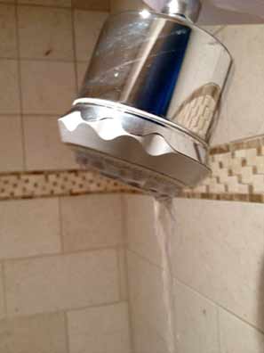 Water leaking out of a chrome showerhead in a tiled shower.