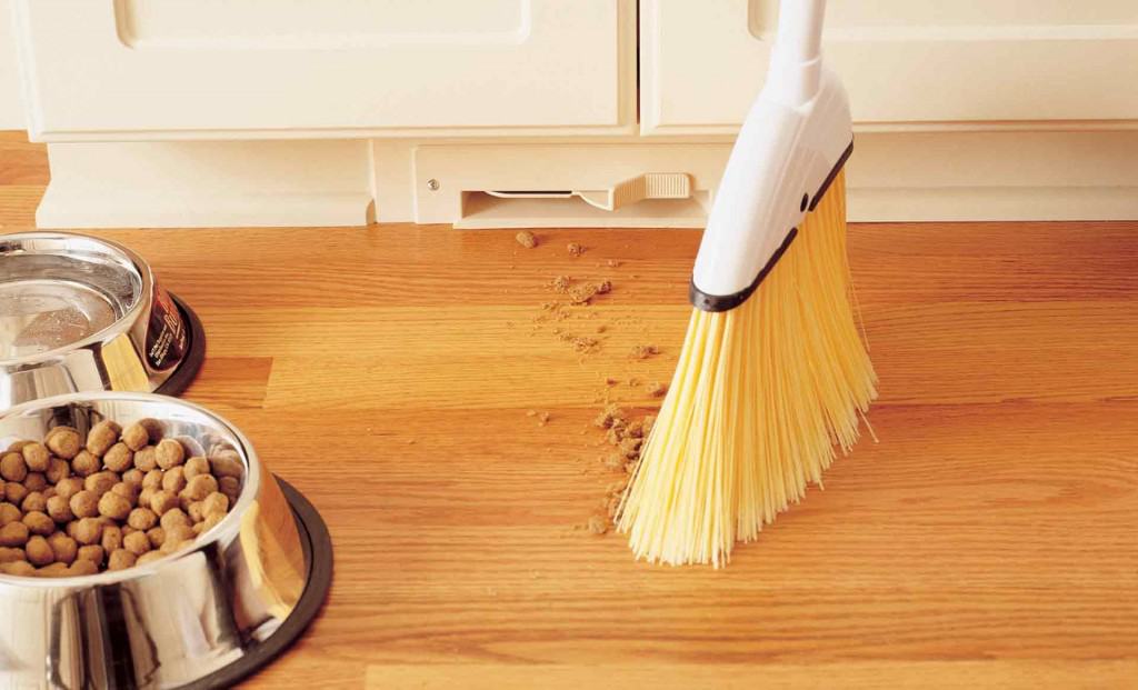Broom sweeping off food particles to an opened baseboard-mounted receptacle.