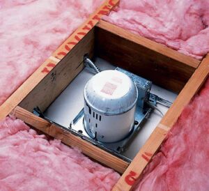 Recessed light between ceiling joists and wood blocking surrounded with insulation.