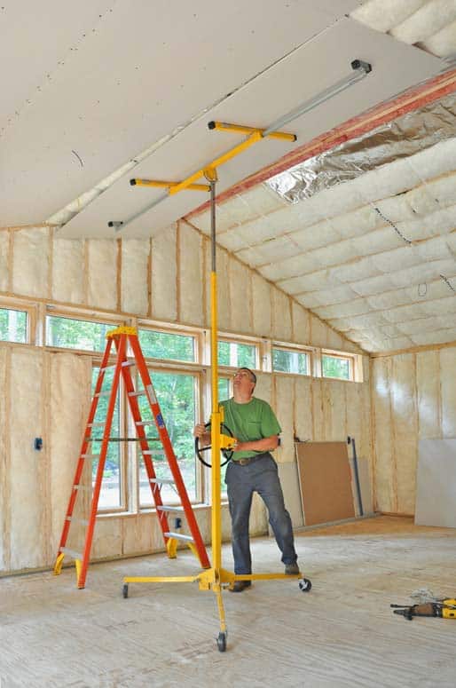 Man installing a dry wall on insulated ceiling panels using a lift.