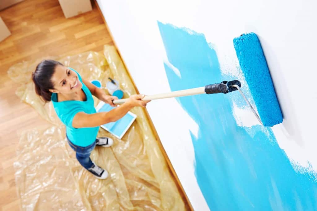 Woman painting a wall using a roller attached to an extension pole.