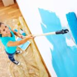 Woman painting a wall using a roller attached to an extension pole.