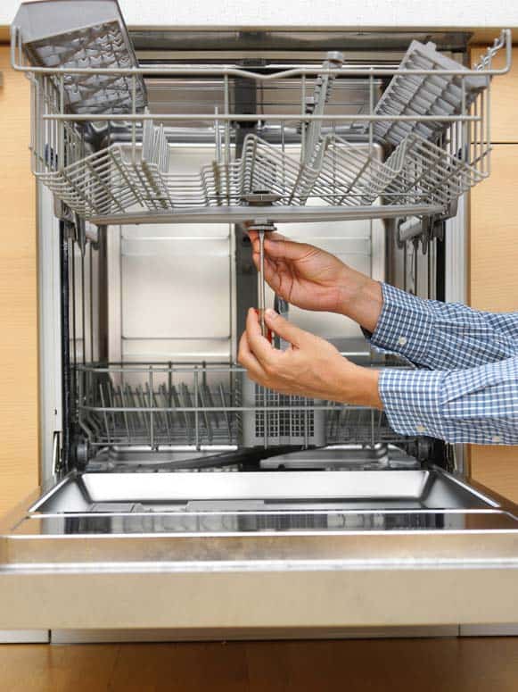 Man’s hand screwing a bolt beneath a dishwasher’s upper spray arm.