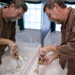 Man unscrewing a toilet sink's faucet parts.