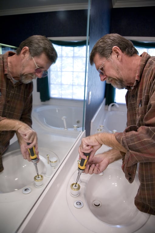 Man unscrewing a toilet sink's faucet parts.