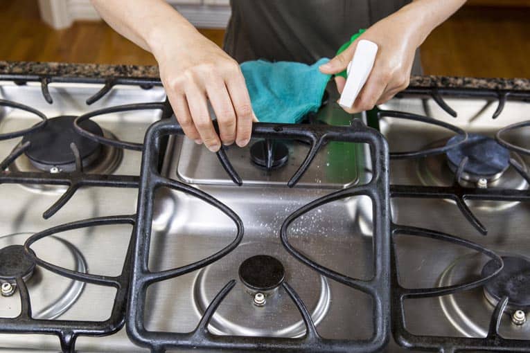 hands using cleaner and cloth to clean burners of gas stove top