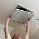 Man removing a furnace filter out from a room's ceiling return-air register.