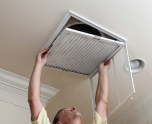 Man removing a furnace filter out from a room's ceiling return-air register.