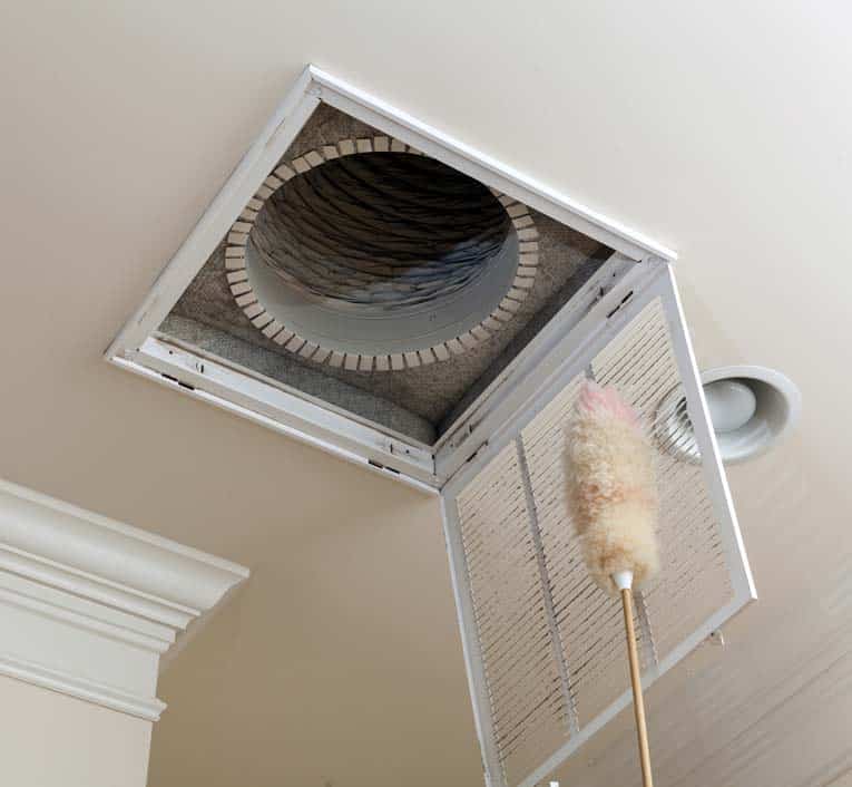 Dusting off a cover grille on a room's ceiling return-air register.