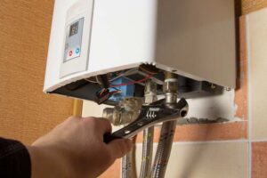 Man's hand wrenching gas and water lines beneath a tankless water heater.