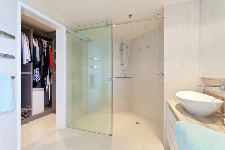 A bathroom’s built-in shower area separated by a top-hung glass sliding door.