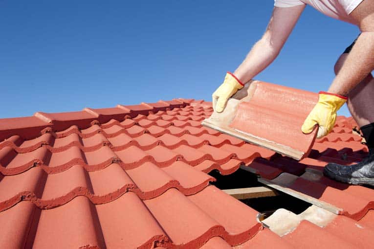 Man's hands holding a pried out red roof tile.