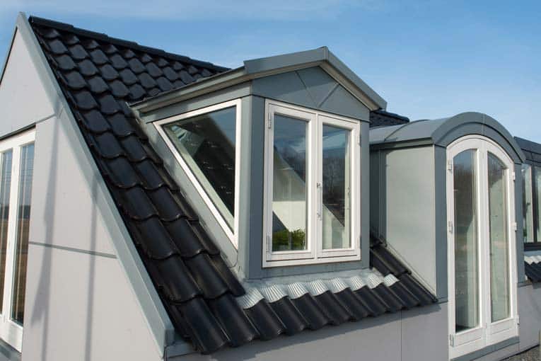 Black tile-like metal roofing including a gable window, and gray gabled and segmental dormers.