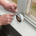 Man's hands cutting an adhesive-backed foam window weather stripping.