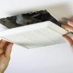 Woman’s hands pulling down a white ceiling vent fan cover.