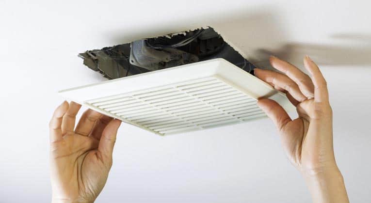 Woman’s hands pulling down a white ceiling vent fan cover.