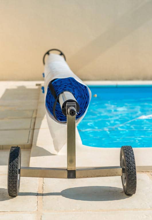 Portable swimming pool cover rolls up on a wheeled carriage and can be moved out of the way when swimmers are in the pool.
